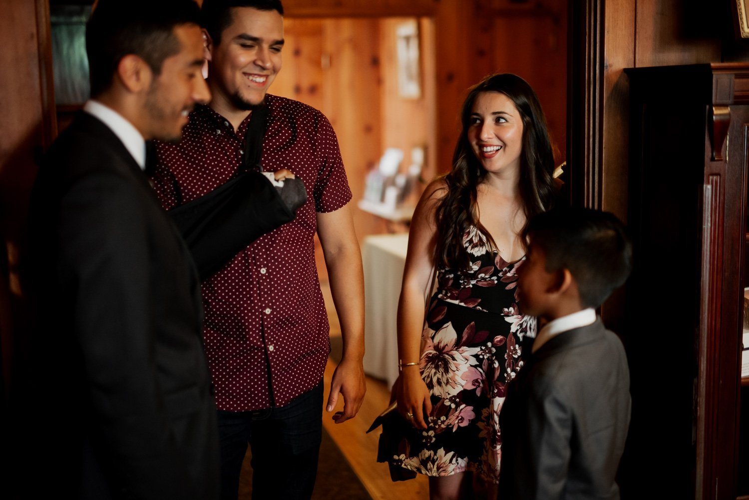 Four people dressed formally, smiling and chatting in a dimly lit wooden room with warm lighting and wooden walls.