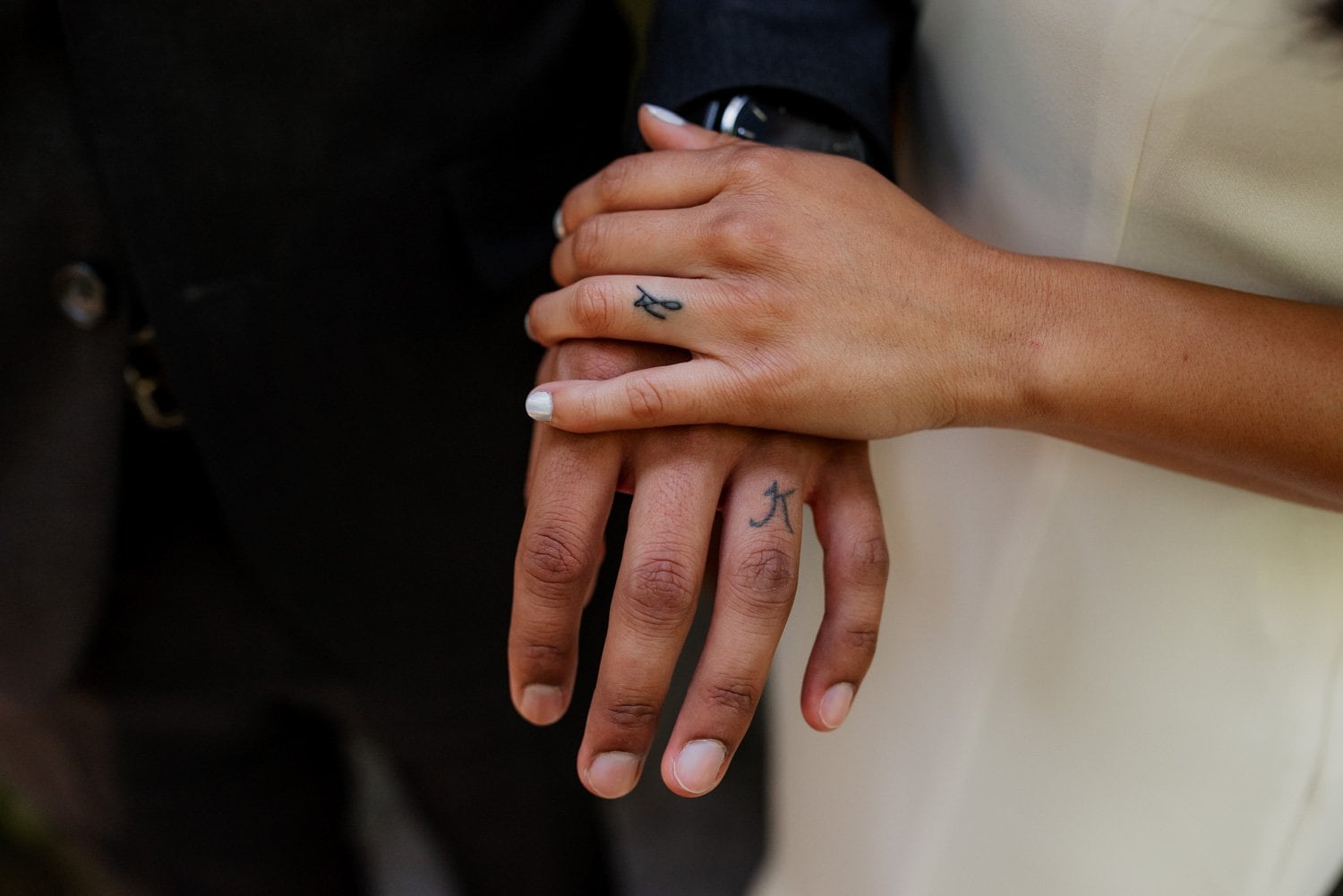 Close-up image of a couples hands with matching tattoos on their ring fingers, set against the greenery backdrop of Leach Botanical Garden during their wedding.