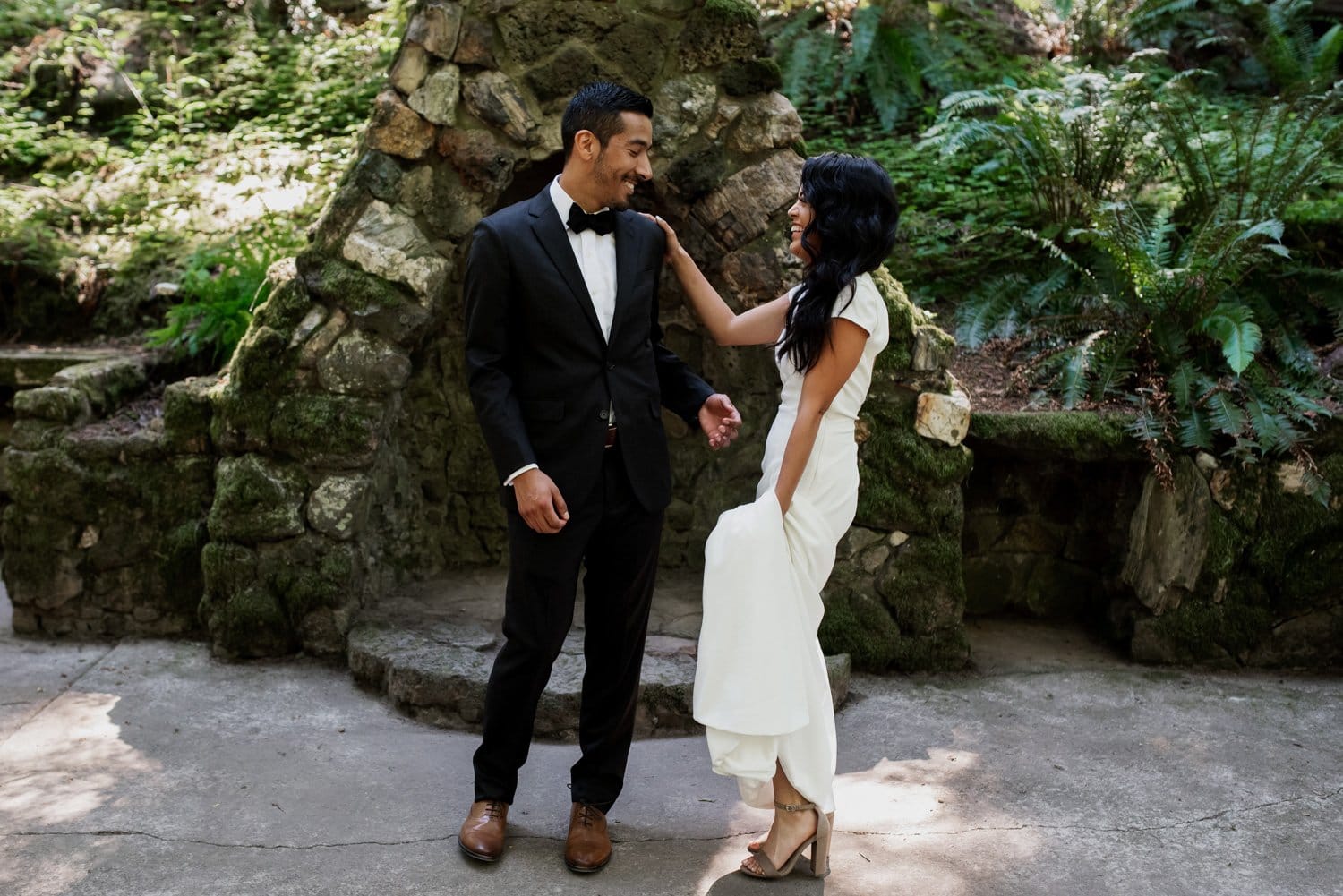 A couple in formal attire shares a joyful moment surrounded by the lush greenery and stone paths of Leach Botanical Garden, eluding happiness and romance.