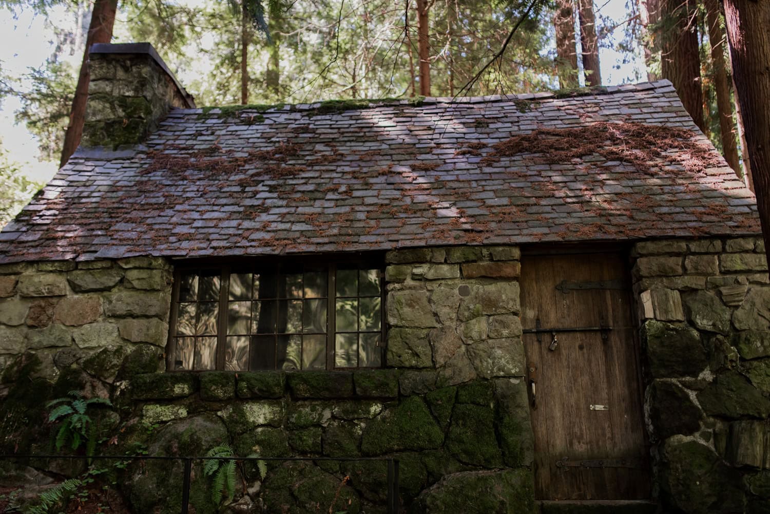 A rustic stone cabin with a shingled roof is situated among tall trees in a forested area, providing a peaceful and secluded atmosphere.