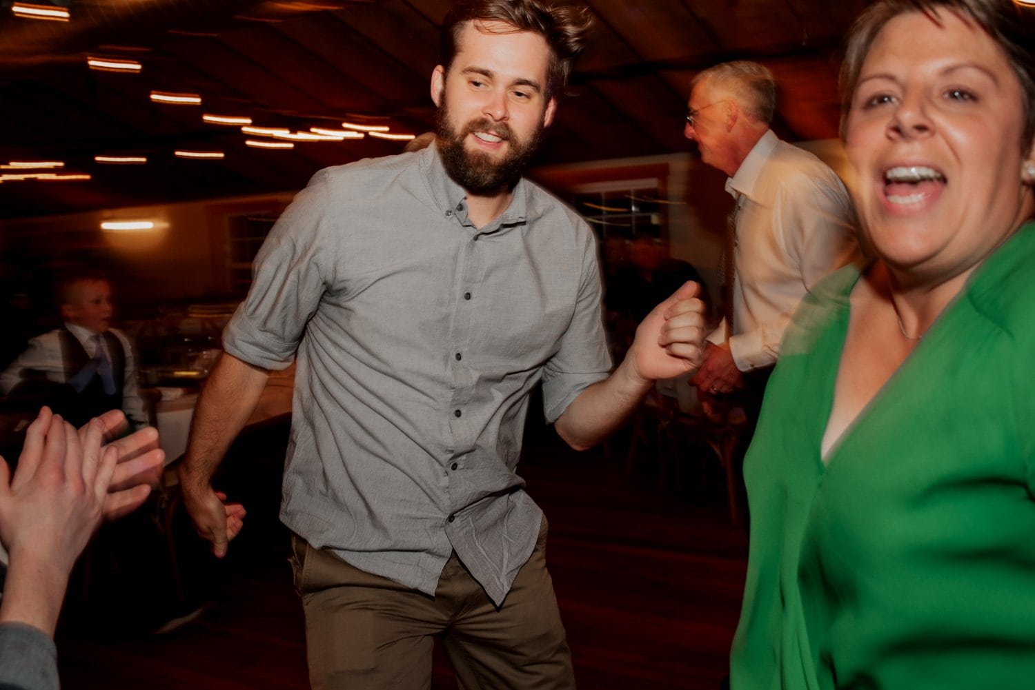 At a wedding held at The Loft at the Red Building, guests danced energetically indoors. A man wearing a gray shirt and a woman in a green shirt are captured mid-dance in blurred motion, reflecting joy in each frame of the wedding photos.