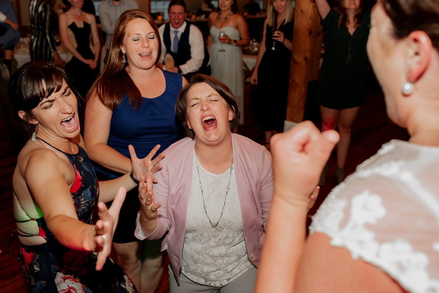 People joyfully singing and dancing at a lively wedding at The Loft at the Red Building, with onlookers in the background.