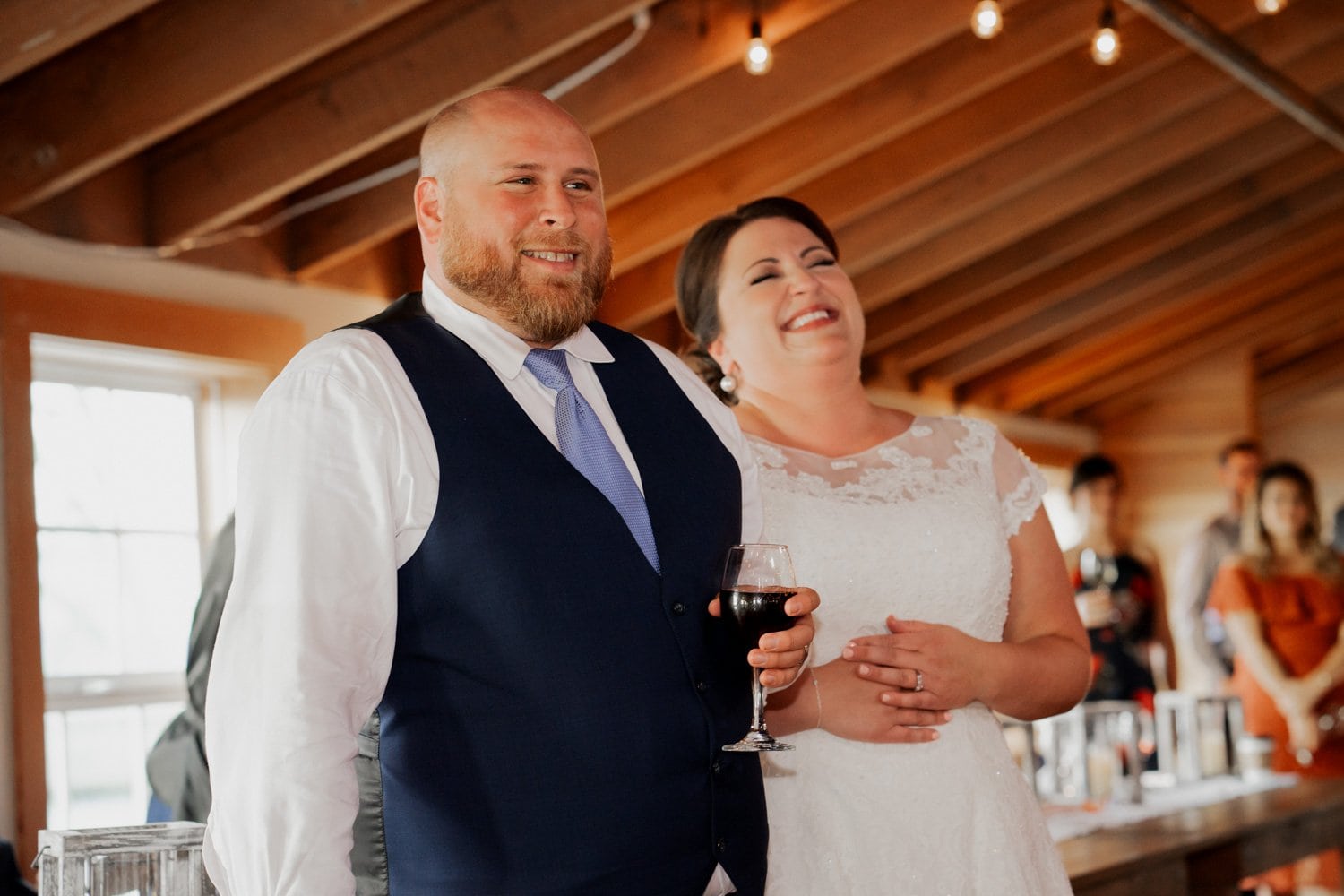 A smiling couple in formal clothing stands together in a warmly lit venue, posing for a wedding photo at The Loft at the Red Building.