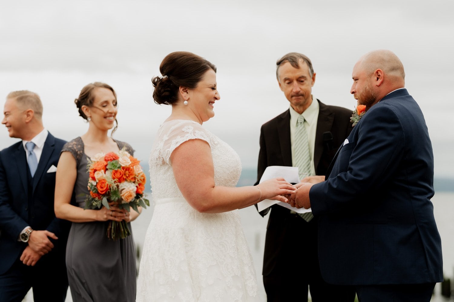 The bride and groom exchange vows outdoors at Astorias Maritime Memorial Park, with a bridesmaid and groomsman standing nearby.