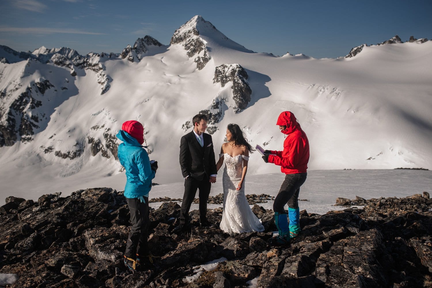 A couple in wedding attire stands together on a snowy mountain, surrounded by an adventurous, wintry landscape during their elopement in Washington's Northern Cascades National Park.