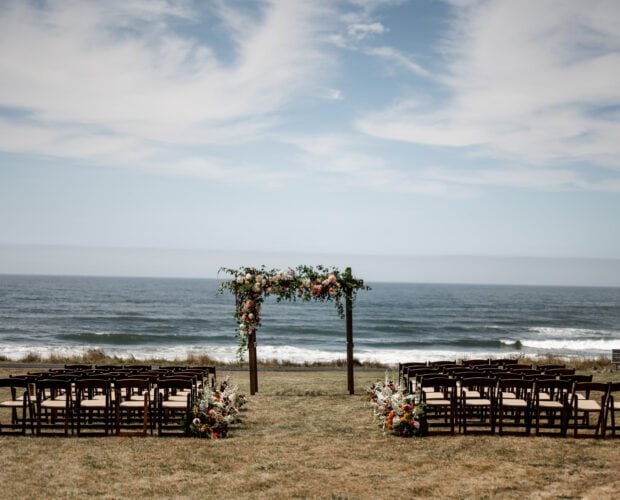 Outdoor wedding setup by the ocean, featuring rows of chairs and a floral arch on a grassy area at the Yachats Inn.