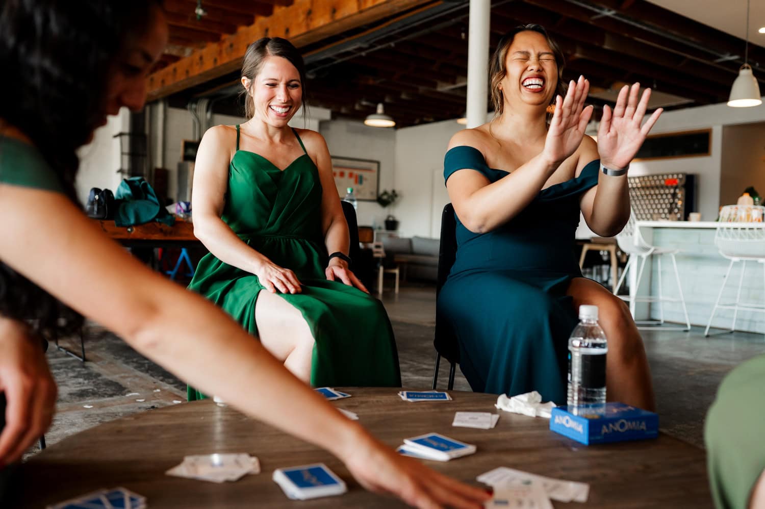 A group of people in green dresses are gathered around a table indoors, laughing and playing a card game during a wedding celebration at Union/Pine.