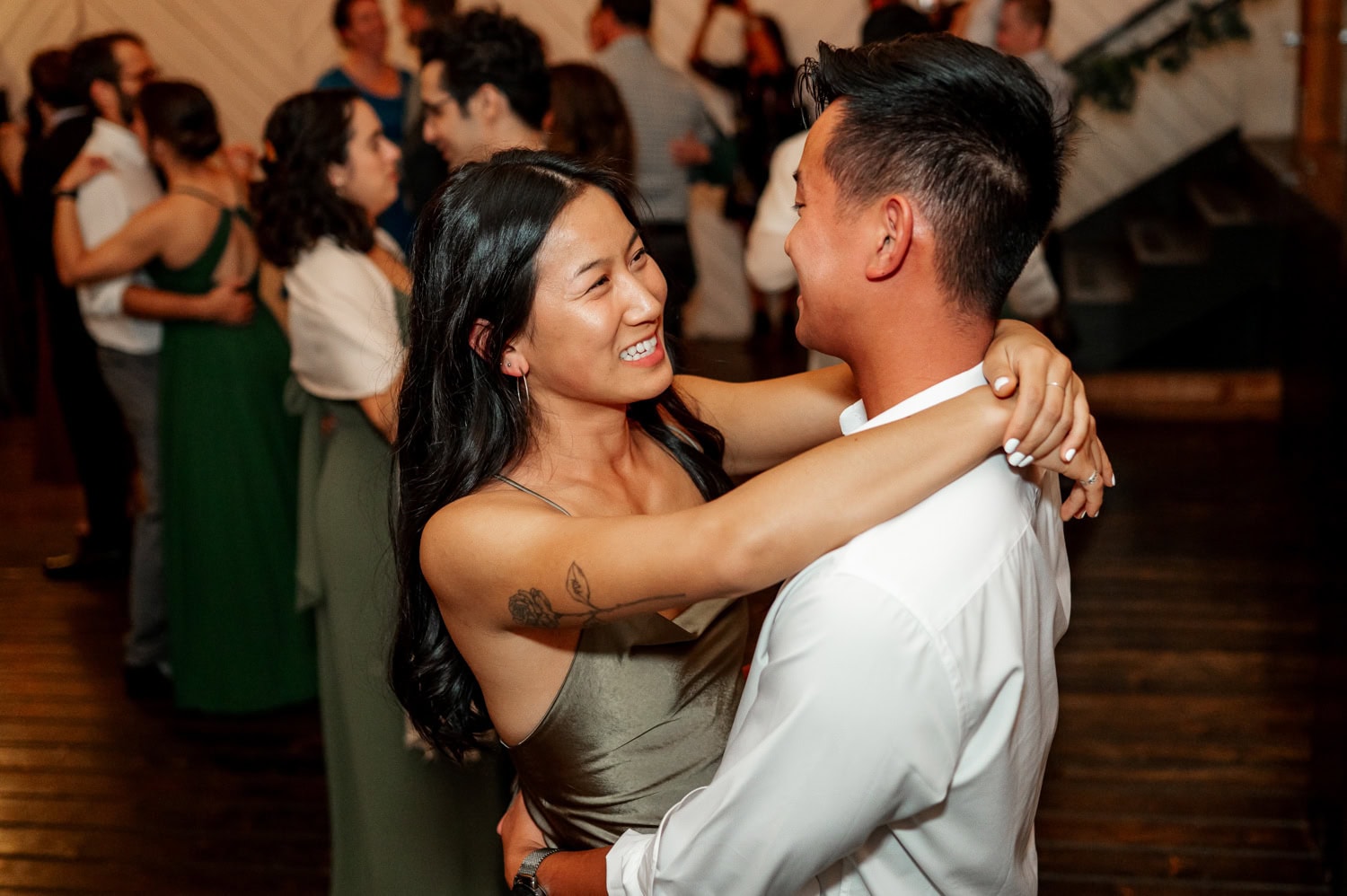 A couple in formal attire dances closely and smiles at each other, surrounded by other joyful couples at a wedding at Union/Pine.