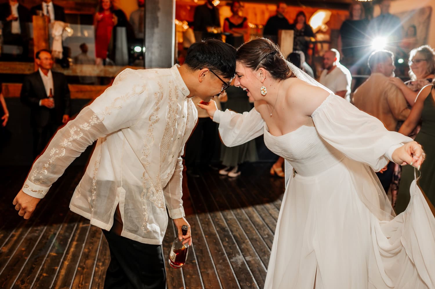 A bride in a white dress and a groom in traditional attire happily dance together at a lively celebration at Union/Pine.