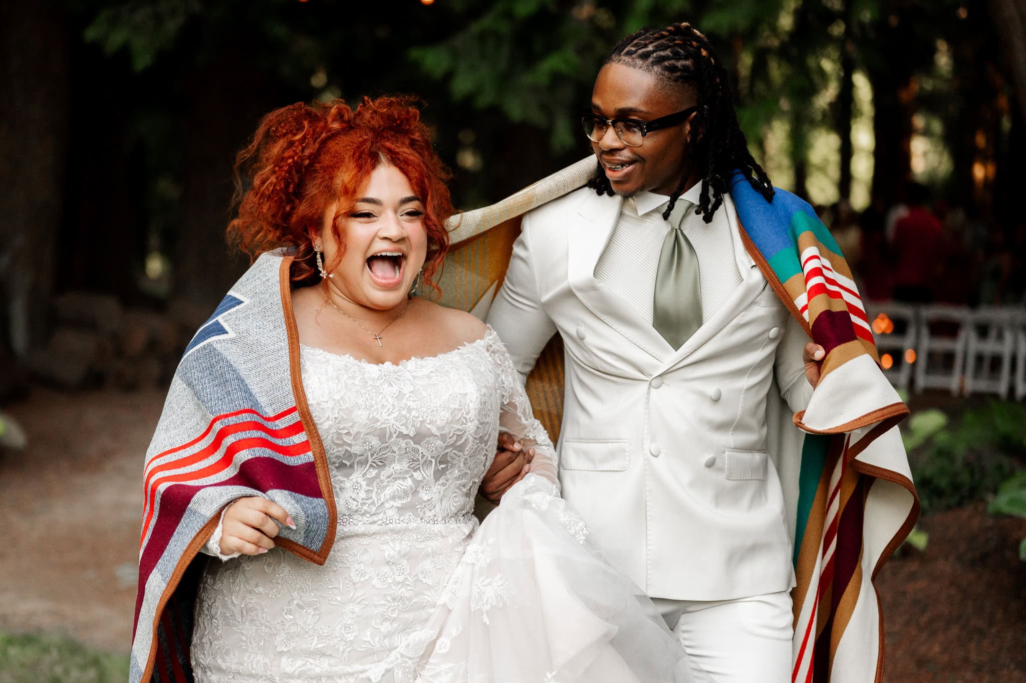 A joyful couple wrapped in a colorful blanket walks outdoors in formal attire, captured by Portland, Oregon wedding and elopement photographer Kyle Carnes.