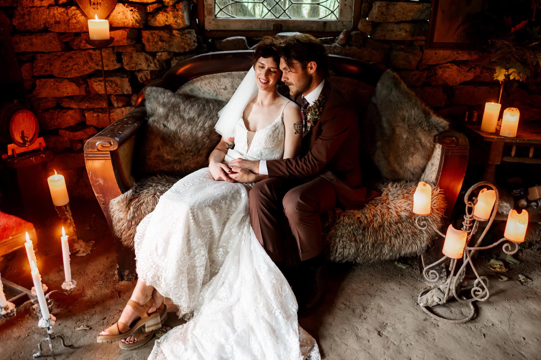 Bride and groom seated on a vintage sofa surrounded by candles in a cozy rustic stone hut at Wilson Farm. The scene, captured by Oregon wedding and elopement photographer Kyle Carnes in Portland, exudes love and warmth.