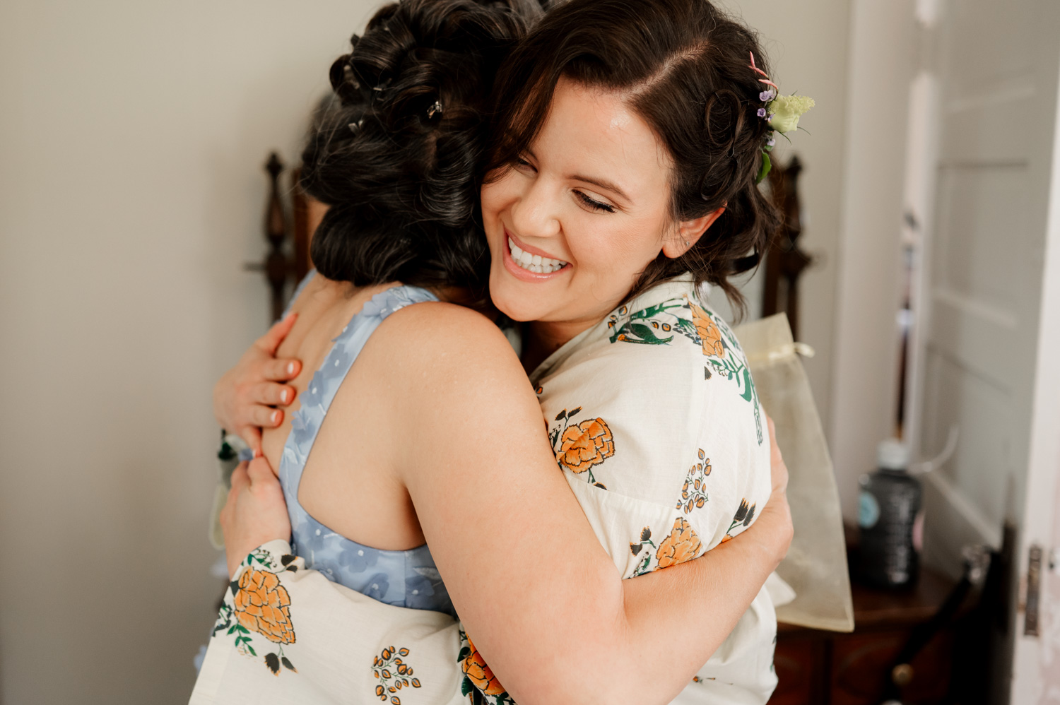 In a cozy indoor setting, two people warmly embrace, their smiles as bright as the floral outfits they wear.