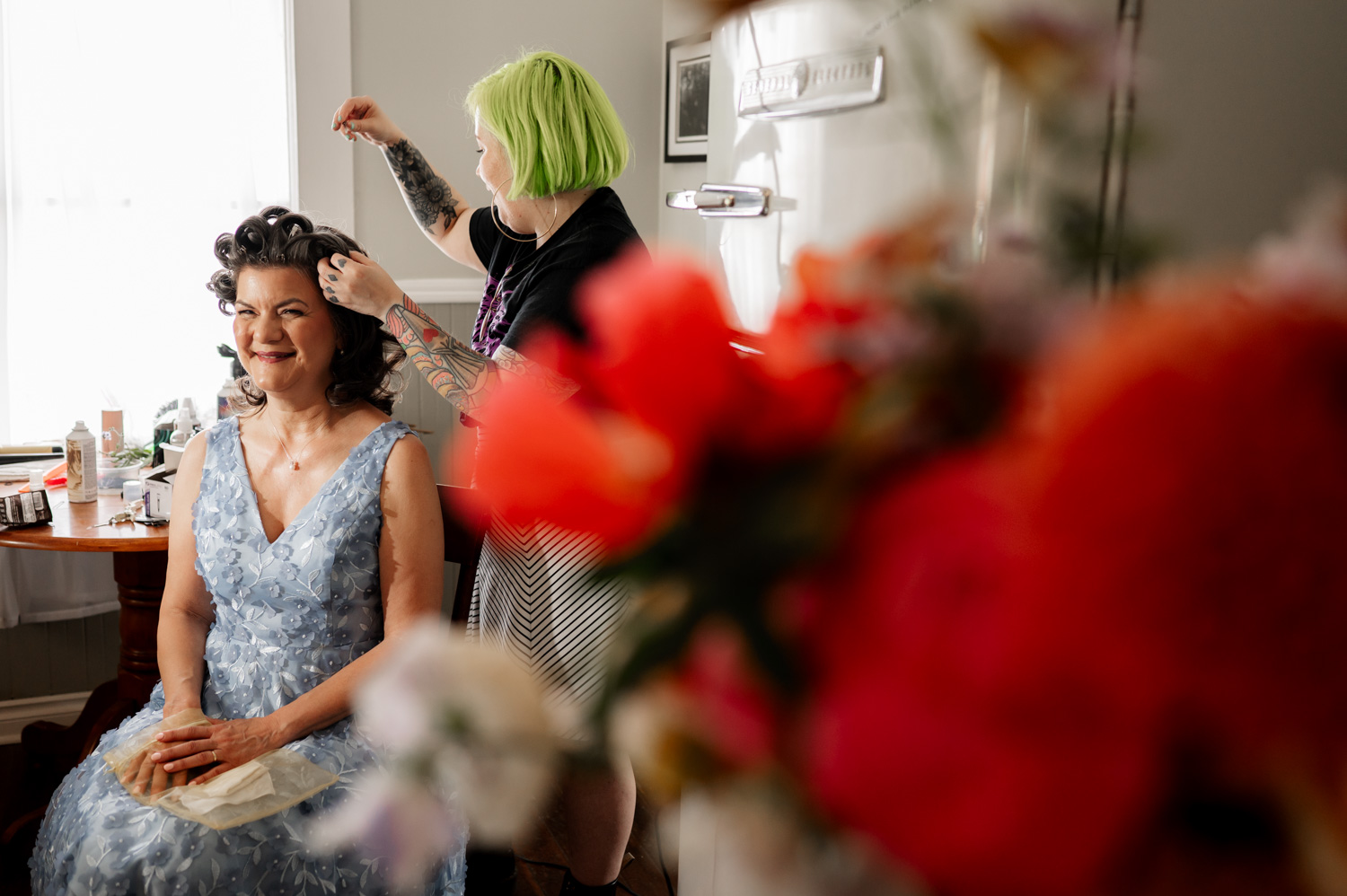 A person in a floral dress is having their hair styled amid vibrant red flowers, capturing a serene moment.