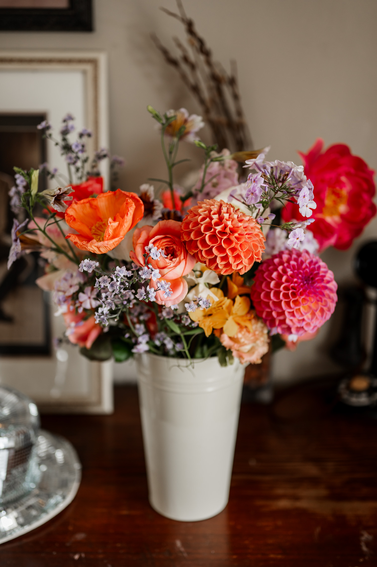 A bouquet of vibrant orange, pink, and purple flowers in a white vase on a wooden table.