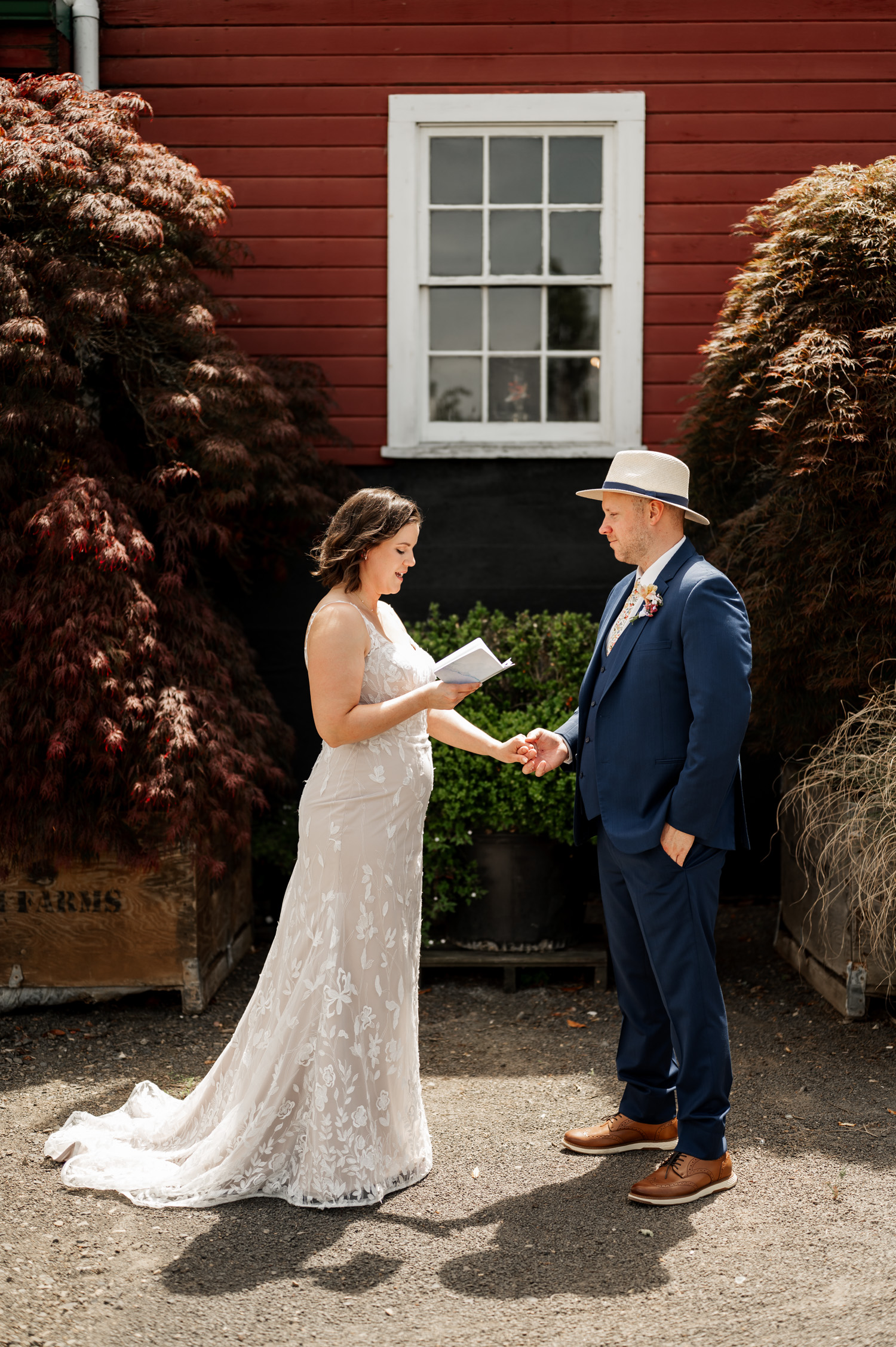 A bride reads her vows to the groom outside at Rossi Farms, with a charming red building and lush trees in the background.