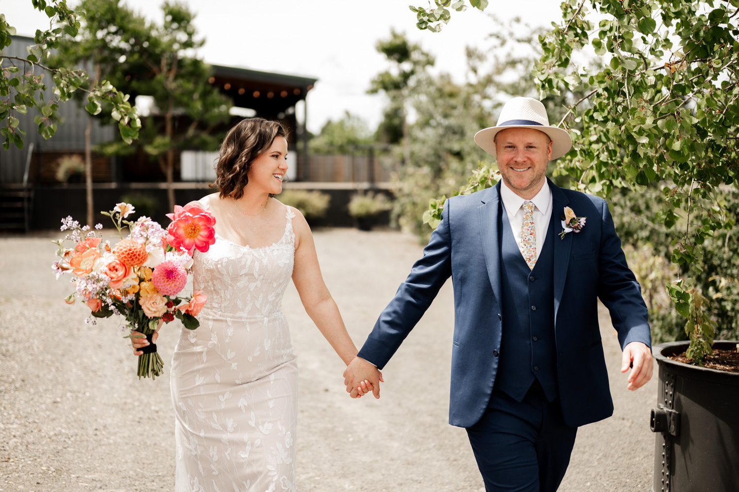 Bride and groom walking hand in hand at Rossi Farms, the bride holding a colorful bouquet and the groom wearing a blue suit.