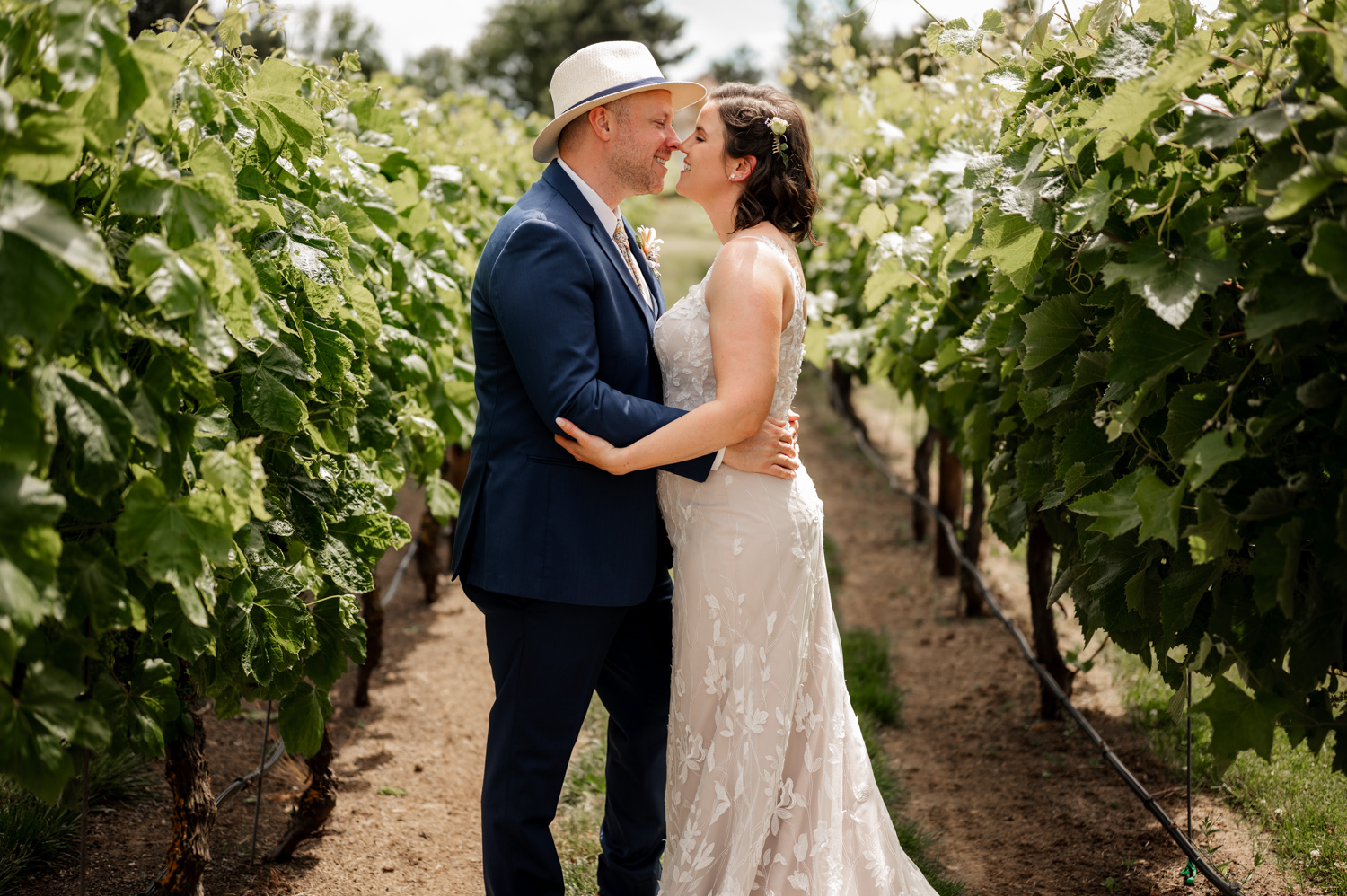 A couple in wedding attire embraces in a vineyard at Rossi Farms, with grapevines surrounding them.