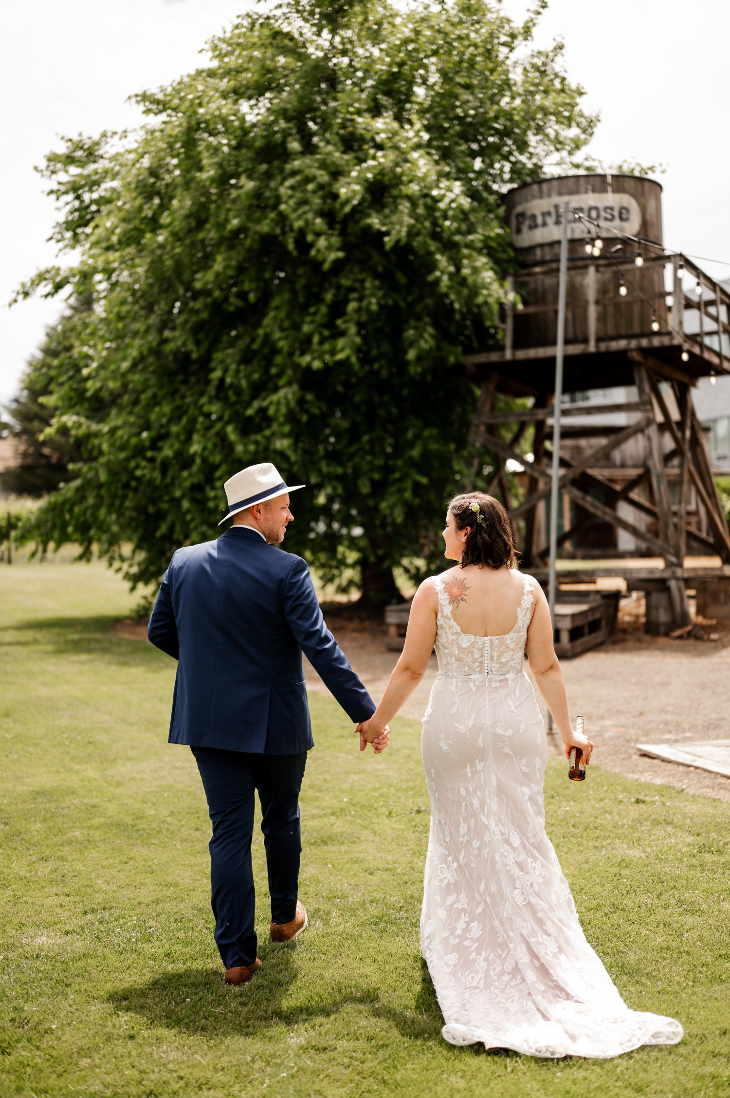 Bride and groom walk hand in hand toward a farmhouse water tower on a sunny day at Rossi Farms.