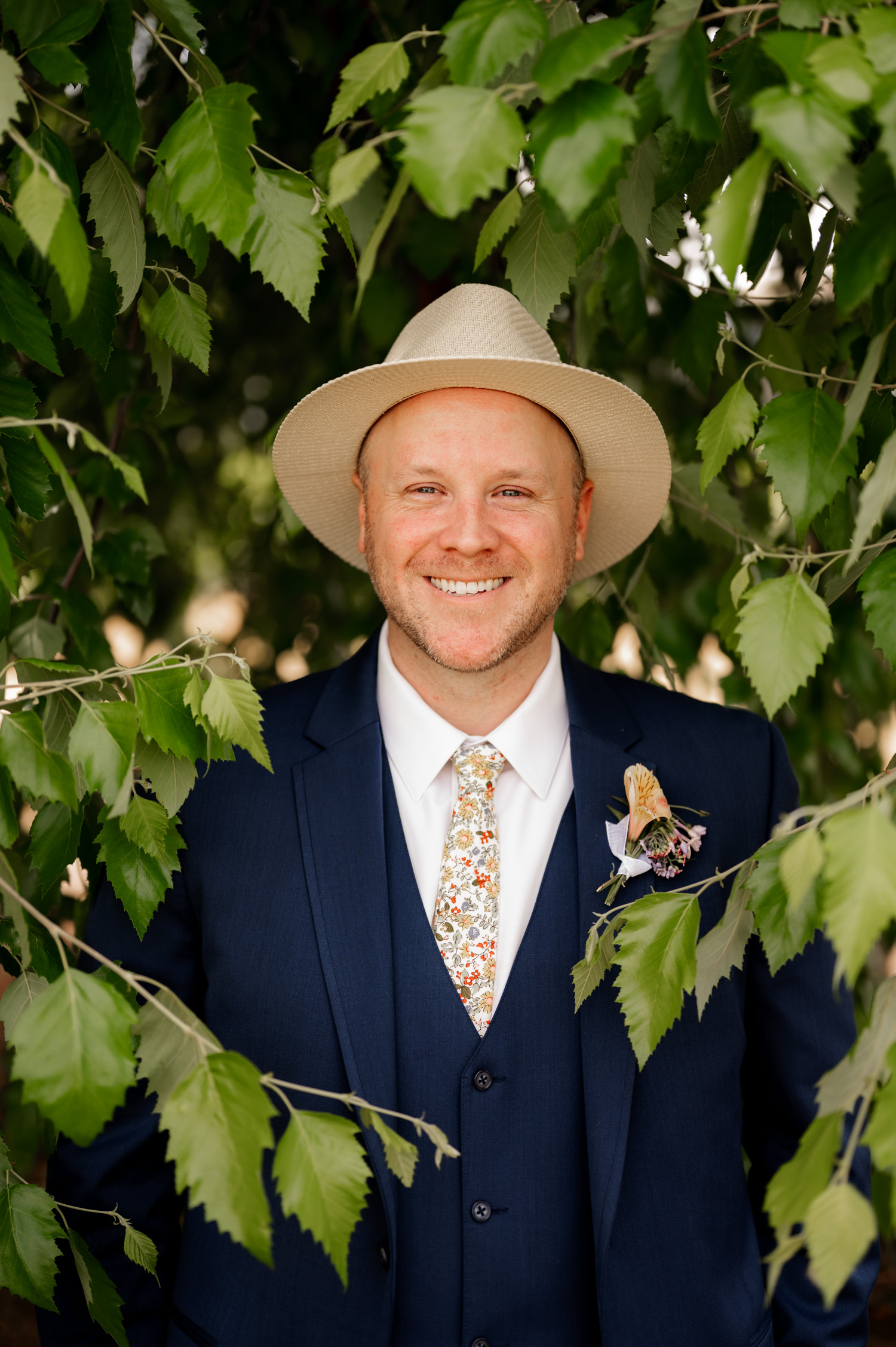 A man in a suit and hat smiles while standing among vibrant green leaves at Rossi Farms.