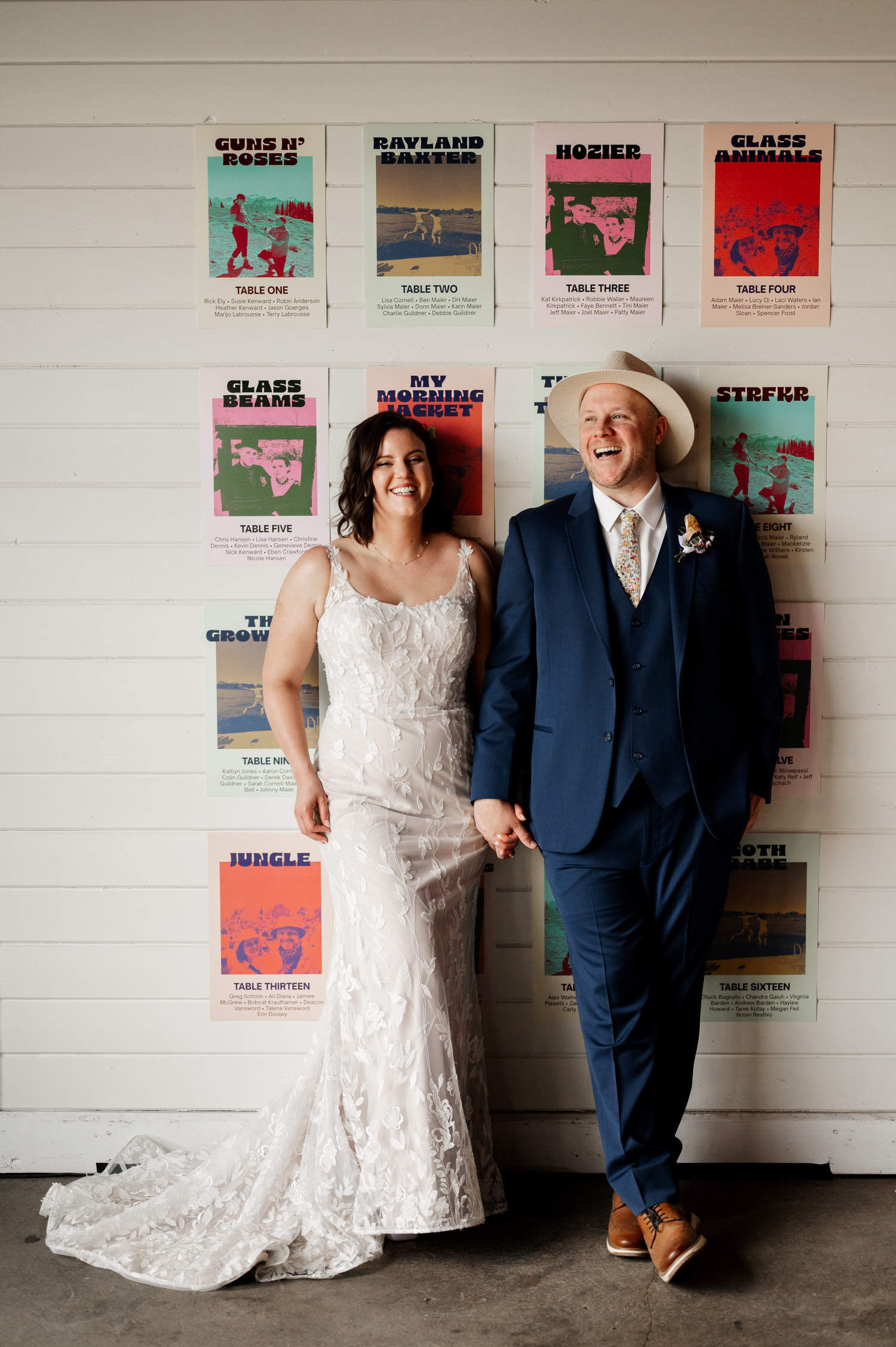 A couple in wedding attire smiles while standing in front of colorful table assignment posters at Rossi Farms.