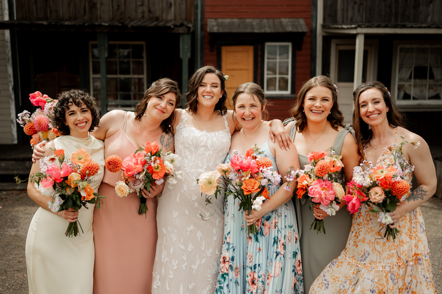 At Rossi Farms, the bride and bridesmaids smile brightly while holding colorful bouquets in a rustic environment.