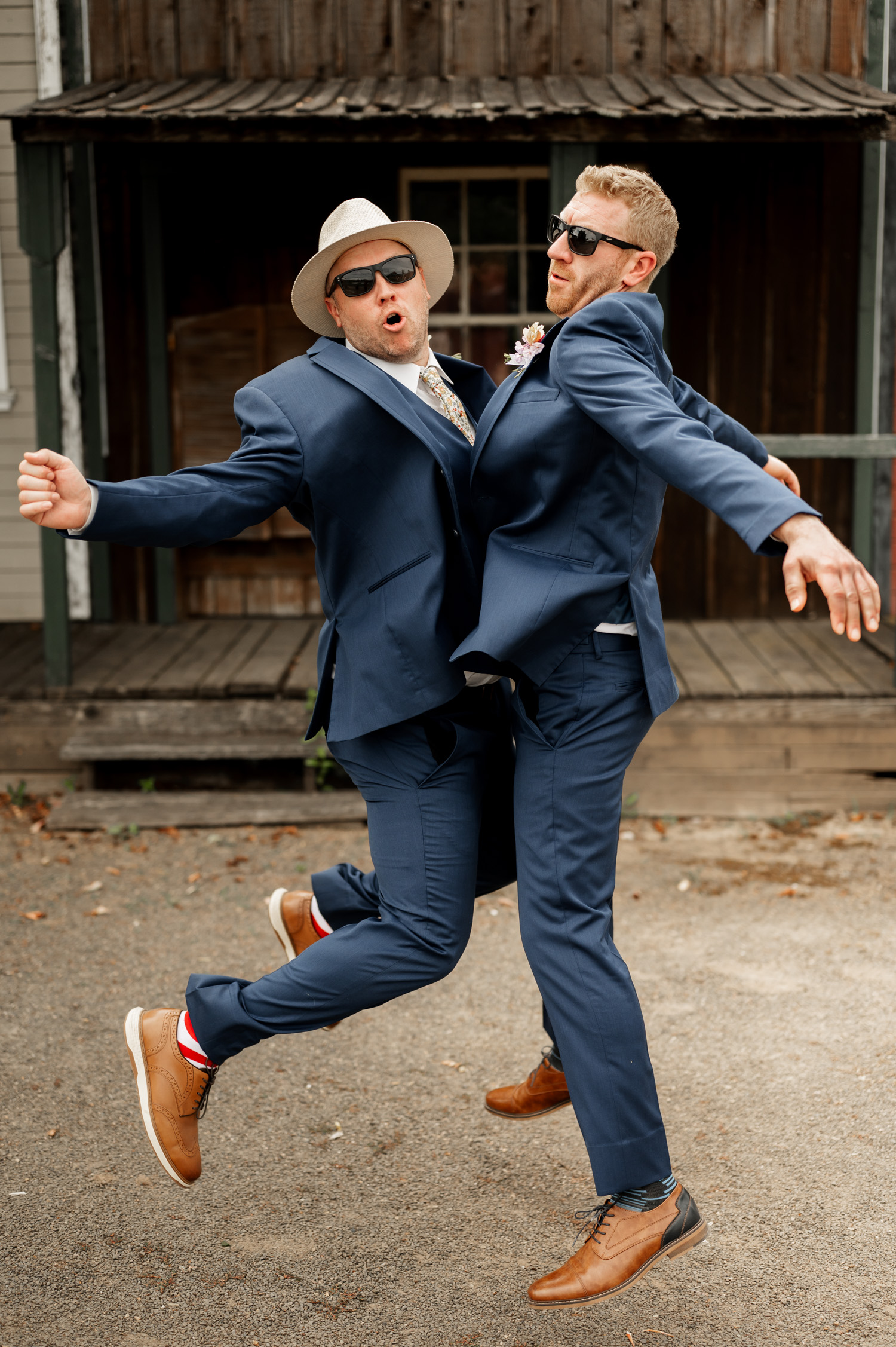 Two men in suits, sunglasses, and hats jump joyfully in the air at Rossi Farms, striking playful poses for the camera.