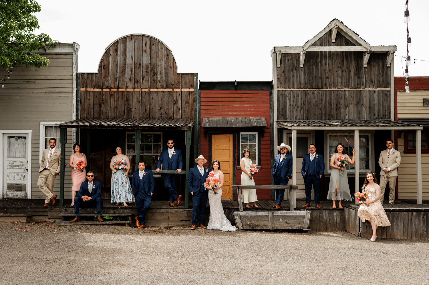 A wedding party poses elegantly in front of rustic buildings at Rossi Farms, with everyone dressed formally and holding bouquets.