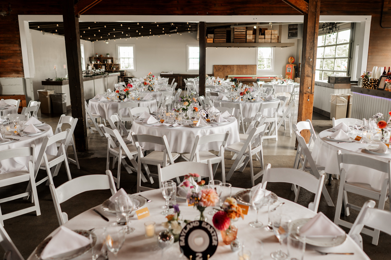 A beautifully set rustic venue at Rossi Farms with round tables, white chairs, floral centerpieces, and twinkling string lights.