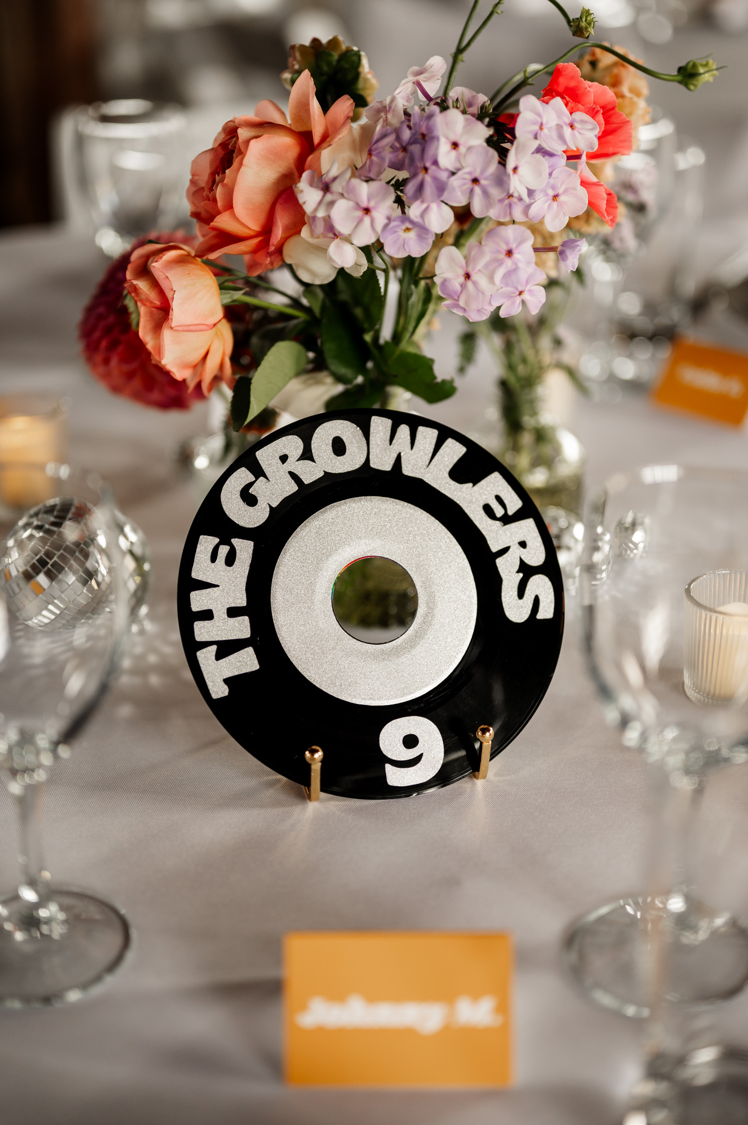 A floral centerpiece and The Growlers vinyl are placed on a table set for a wedding at Rossi Farms. Place cards are arranged around the display.