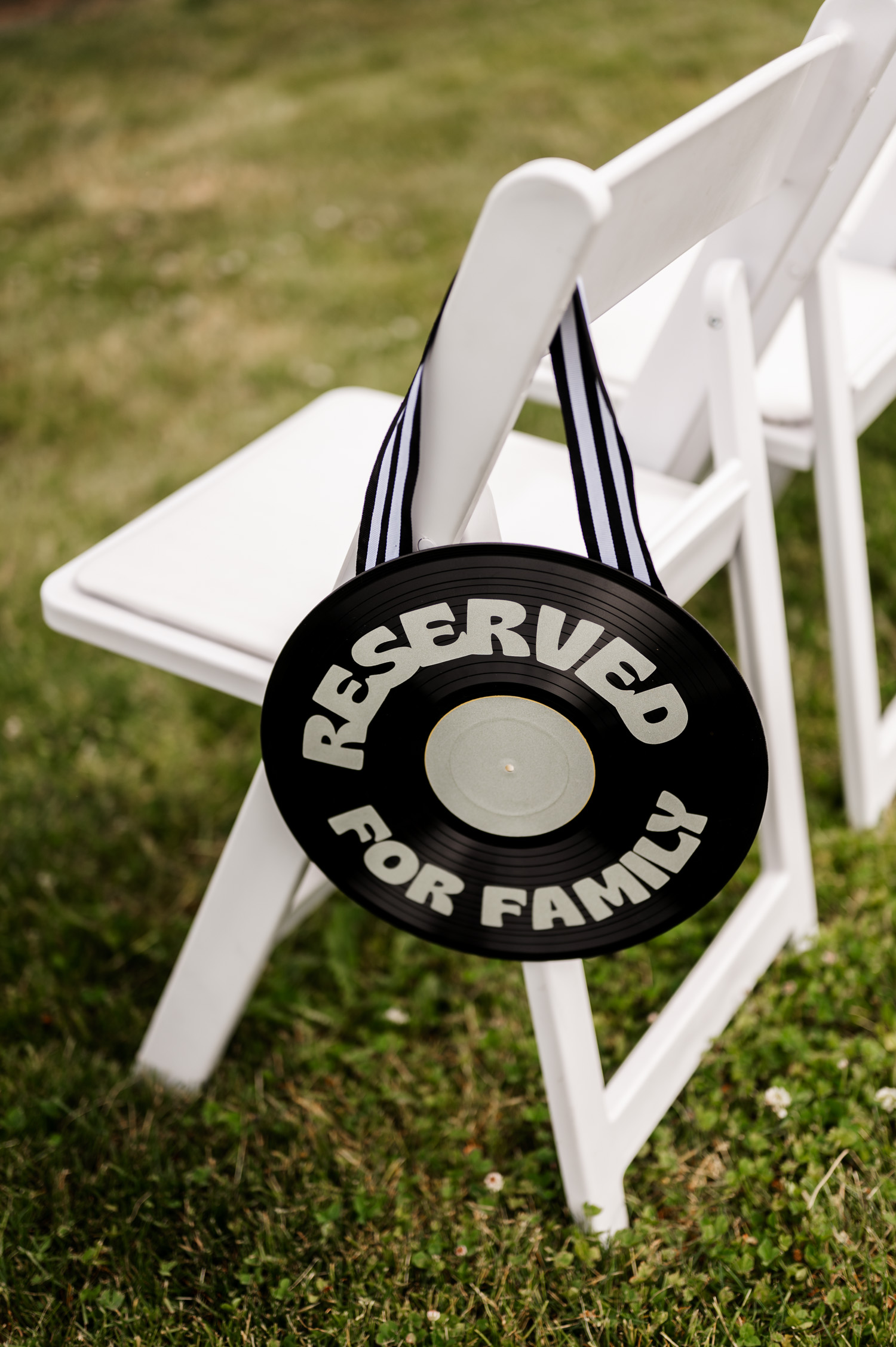 A black vinyl record with Reserved for Family text is displayed on a white folding chair in the green grass at Rossi Farms.