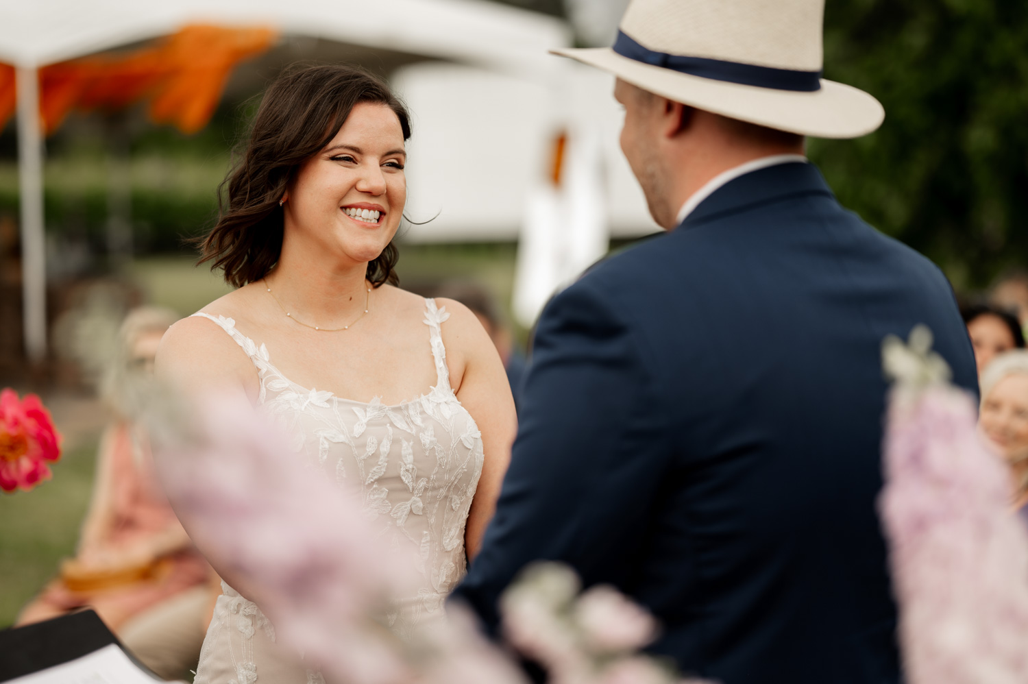 During their outdoor ceremony at Rossi Farms, the bride smiles joyfully at the groom, capturing a perfect moment in their wedding photos.