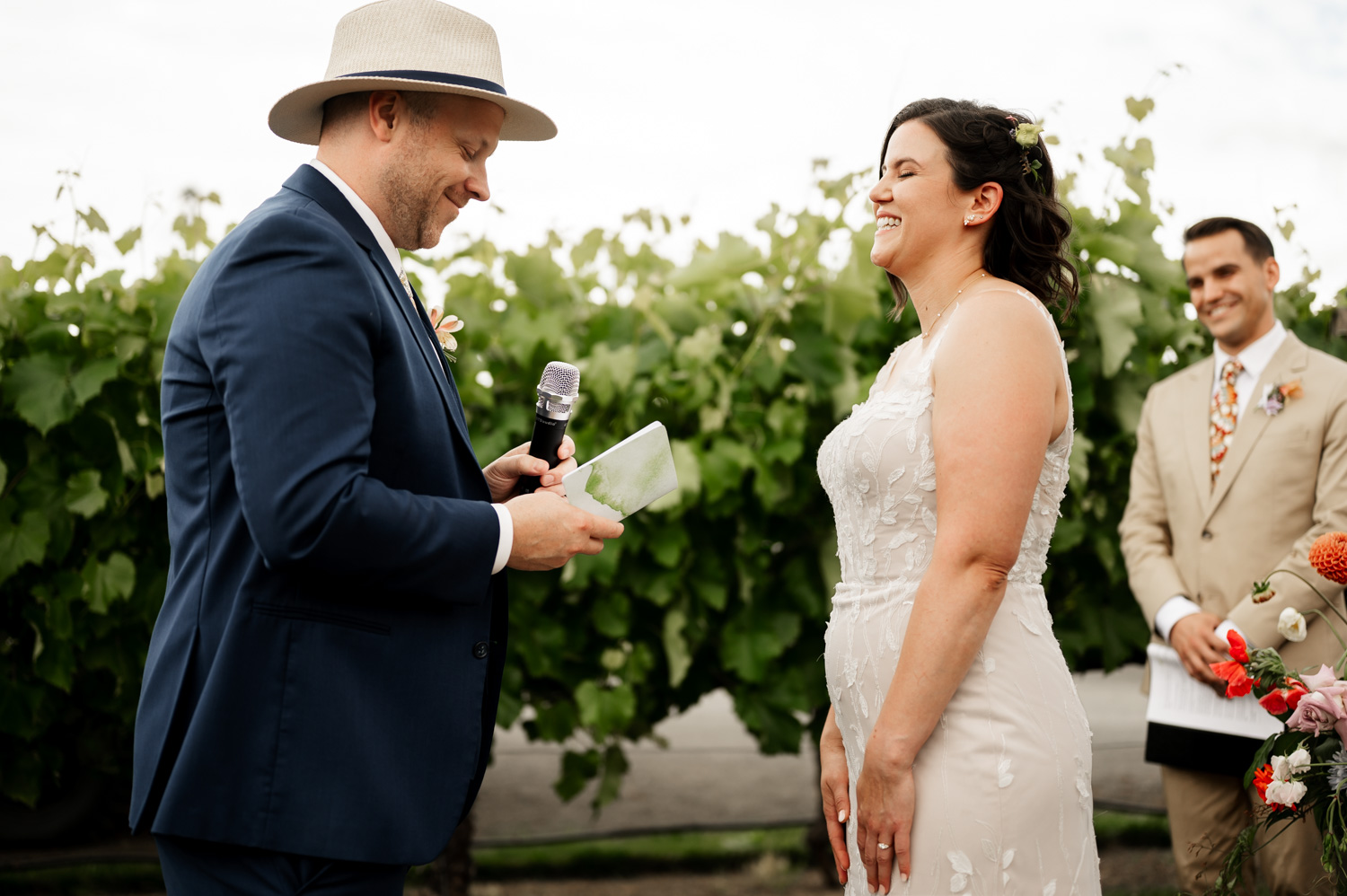A groom reads vows to a smiling bride outdoors at Rossi Farms, with the best man standing nearby in the vineyard background.