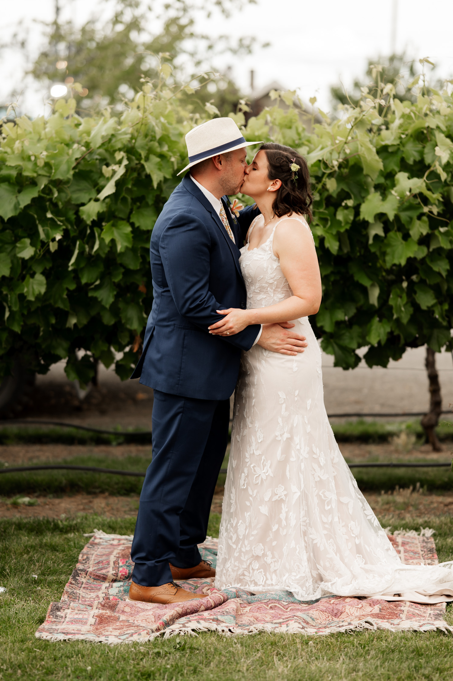 A bride and groom share a kiss on a patterned rug surrounded by lush green vines at Rossi Farms.