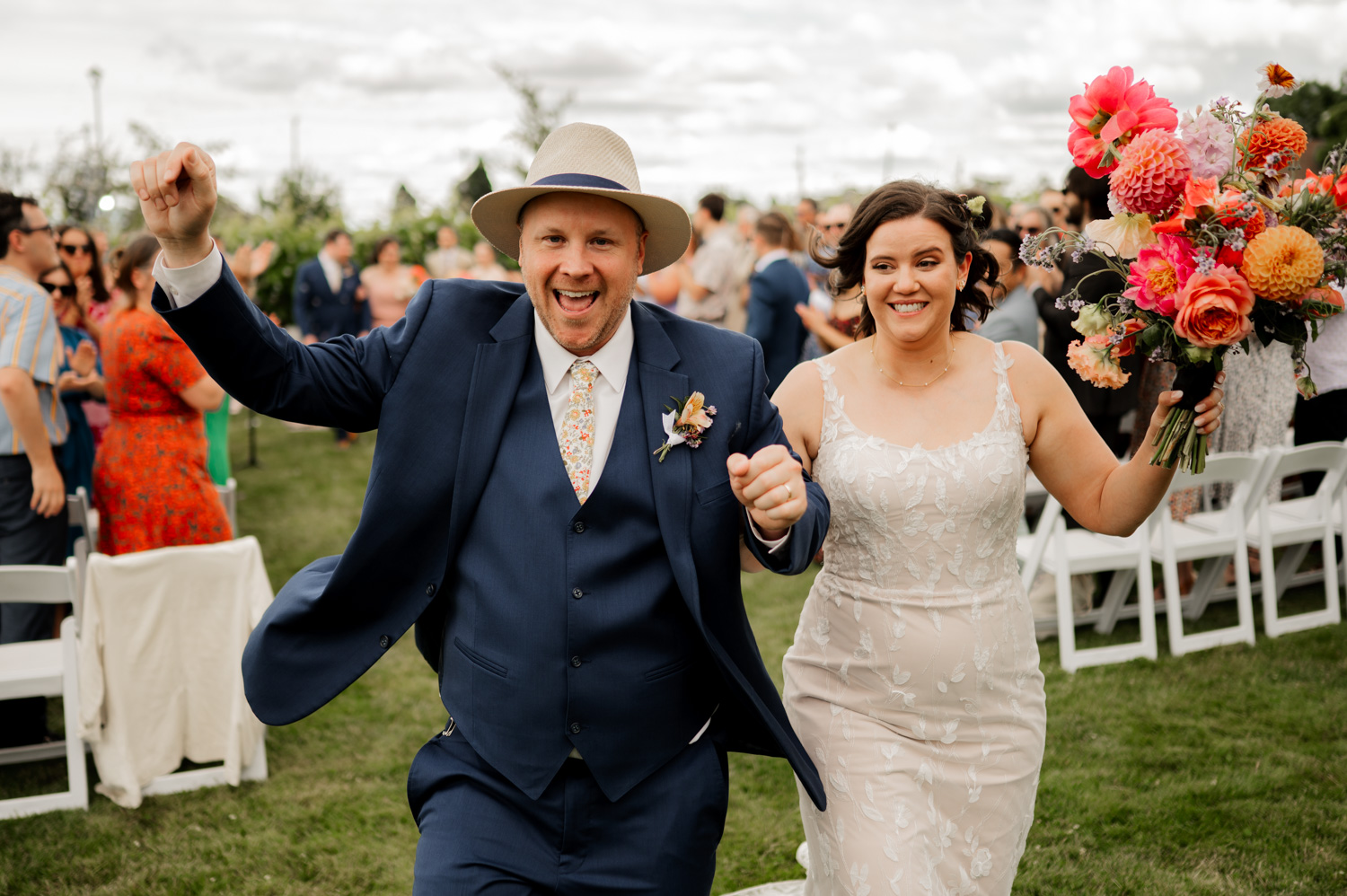 A newlywed couple celebrates at an outdoor wedding at Rossi Farms. They are surrounded by guests who are taking photos to capture the moment.