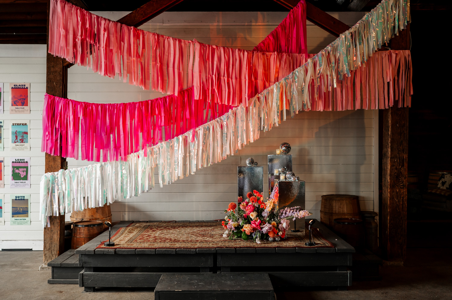 A small stage at Rossi Farms is decorated with colorful ribbons and a beautiful floral arrangement. Silver disco balls add a touch of sparkle to the rustic setting, creating an eye-catching backdrop for wedding photos.
