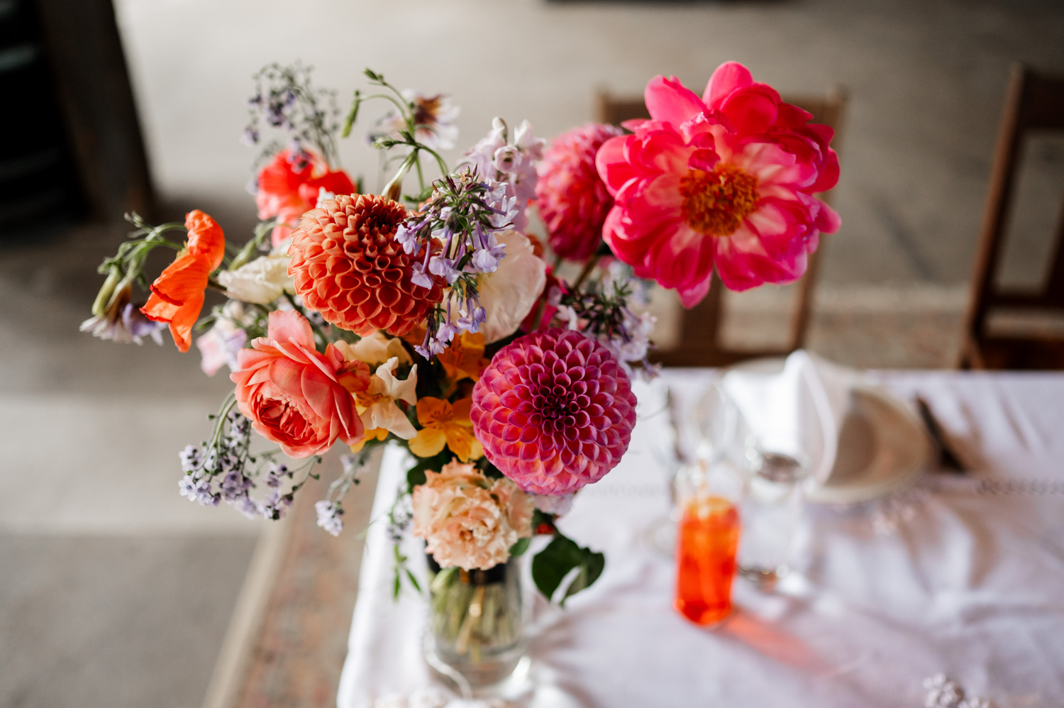 A vibrant bouquet with pink, orange, and purple flowers is displayed on a white tablecloth.
