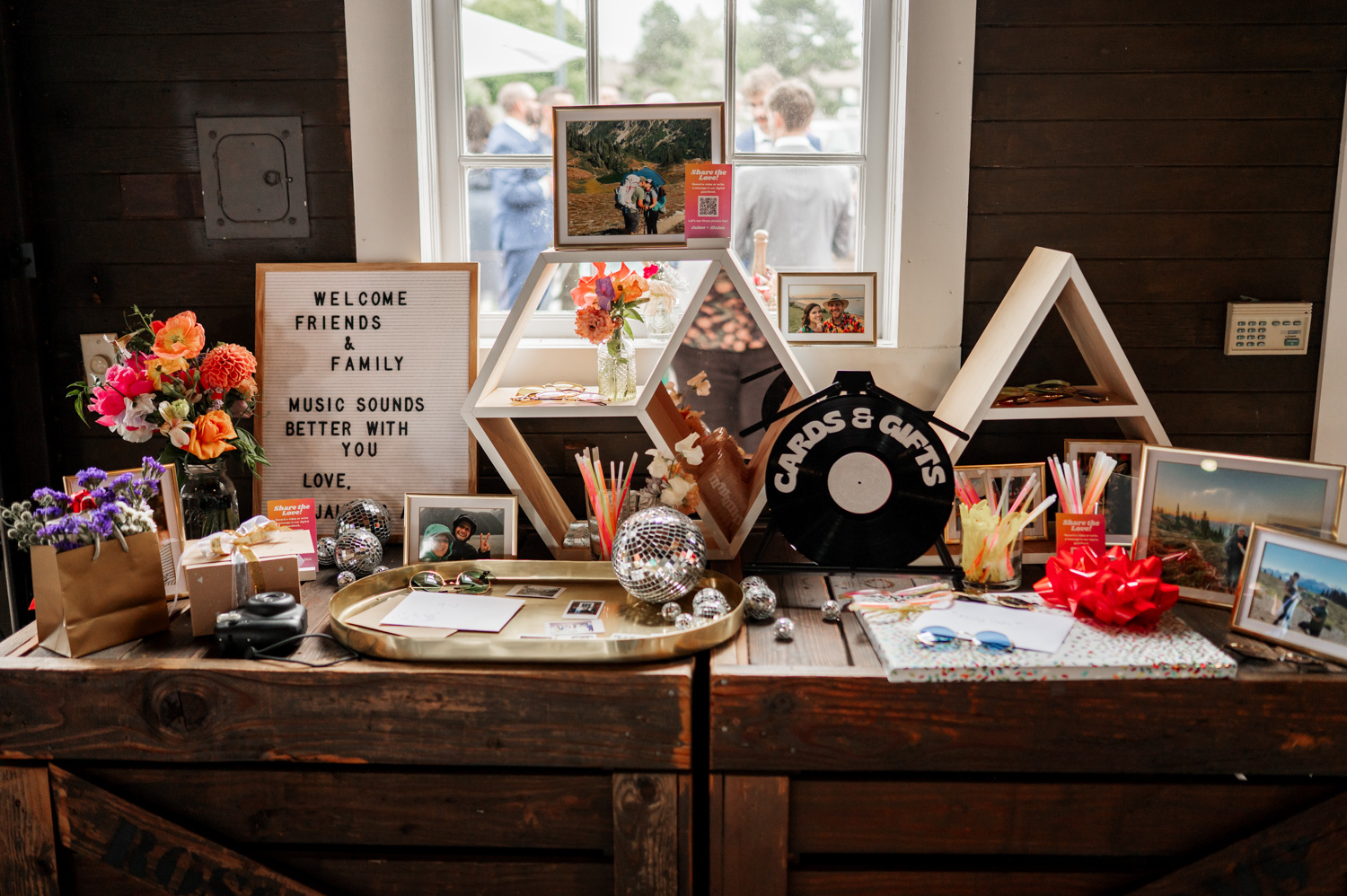 A decorative display table features vibrant flowers, colorful cards, and vinyl record decor alongside cherished wedding photos from Rossi Farms.