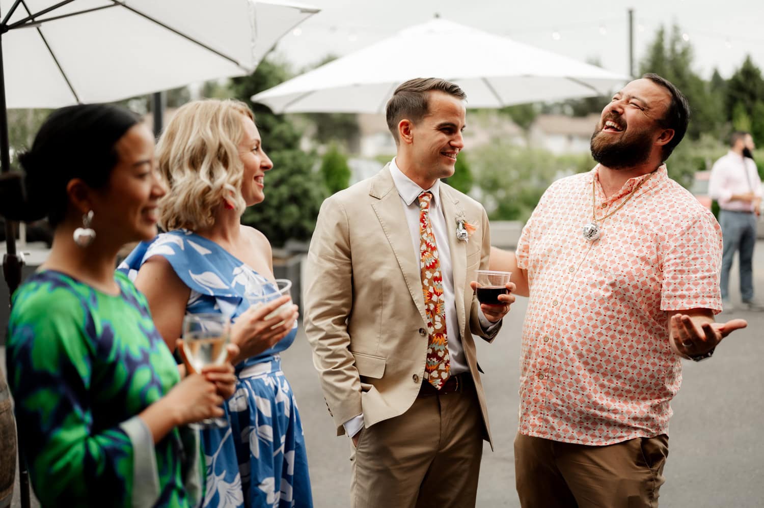 Four people smiling and talking outdoors, each holding a drink, with white umbrellas providing shade on a sunny day at Rossi Farms.