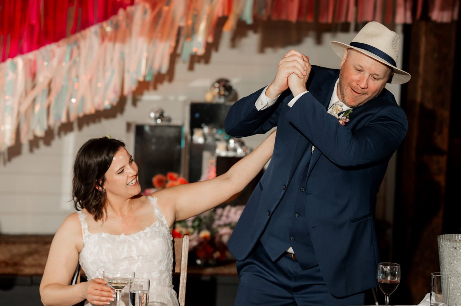At Rossi Farms, the bride playfully holds the grooms arm while he smiles, surrounded by wine and elegant decorations.