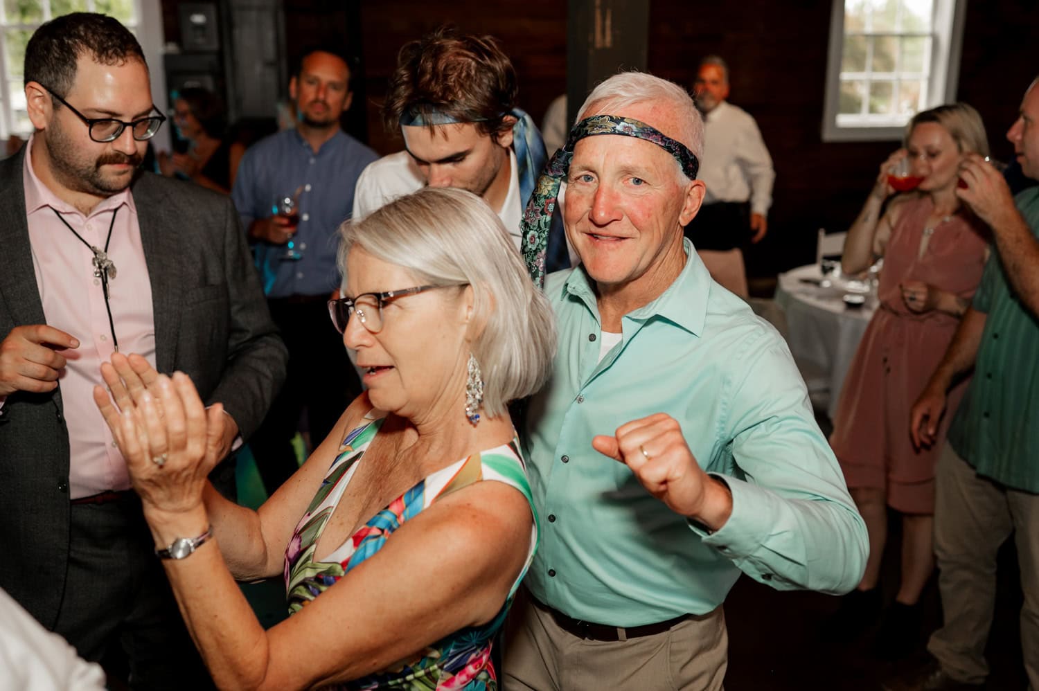 A lively scene of people dancing with joy at a Rossi Farms wedding, wearing casual and colorful outfits. The atmosphere is festive and vibrant, filled with laughter and movement.