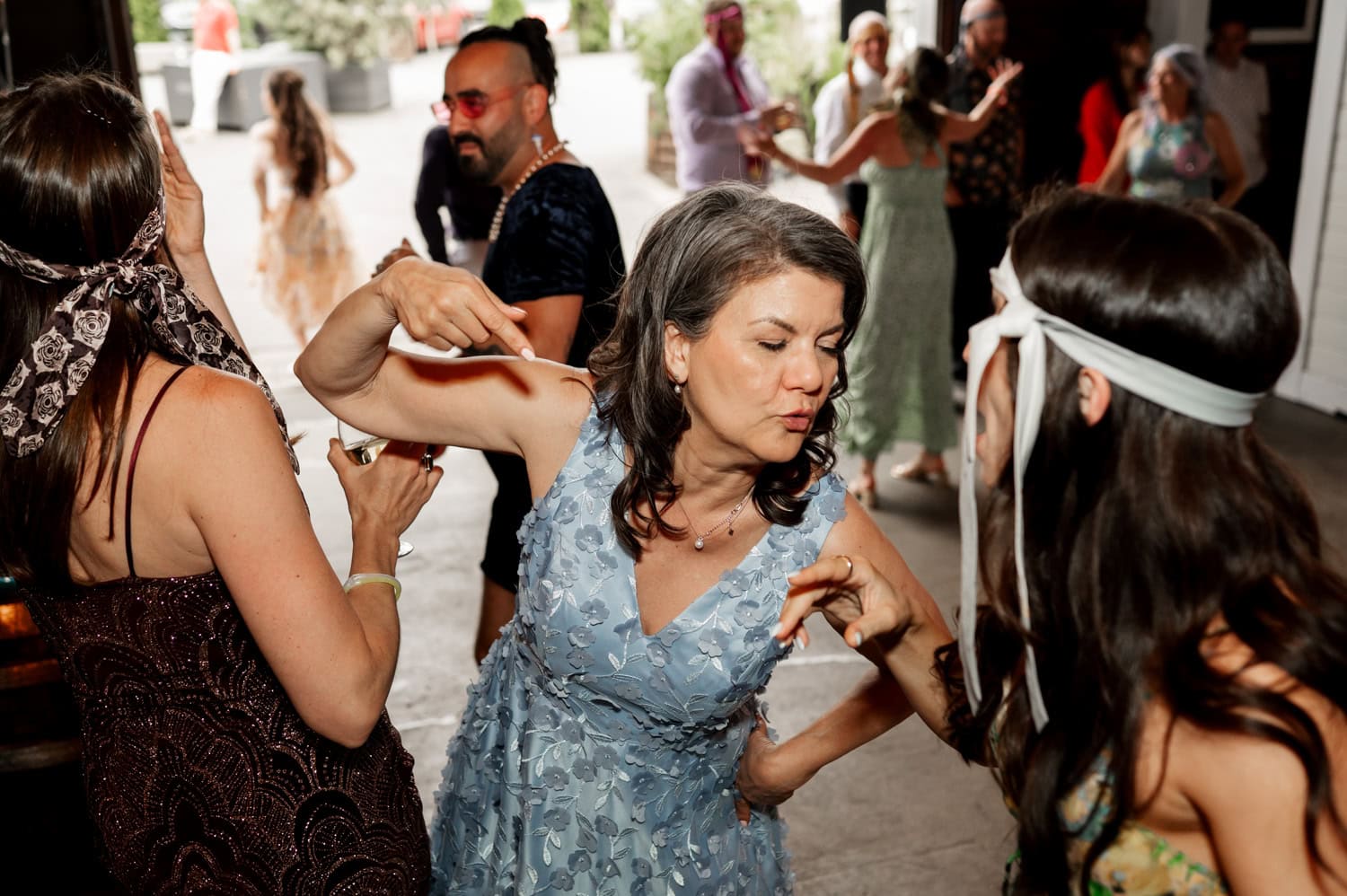 People dancing energetically at a party, wearing festive attire and headbands, in a lively indoor setting.
