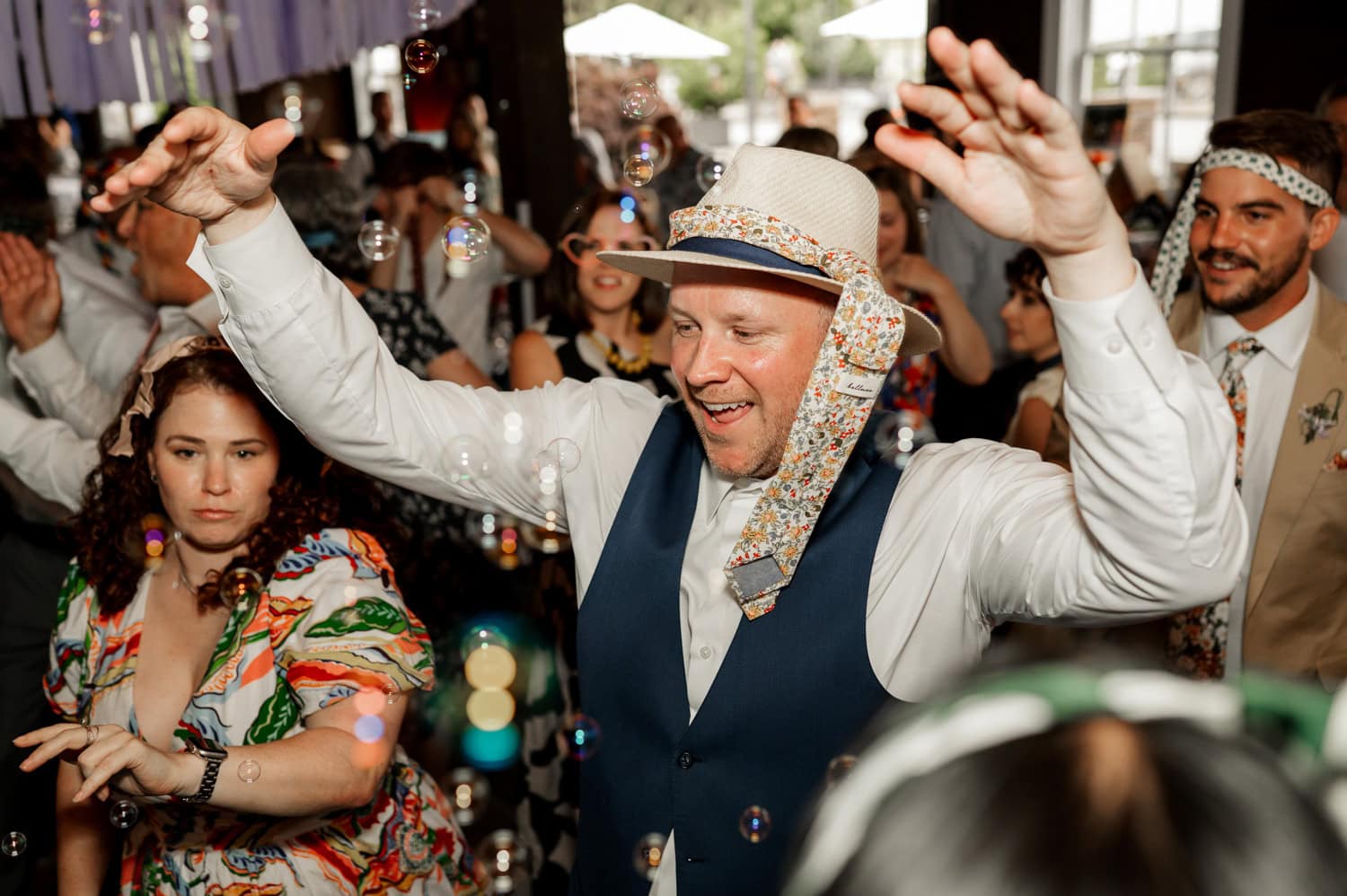 A man in a hat dances happily under a shower of bubbles at Rossi Farms during a wedding celebration.