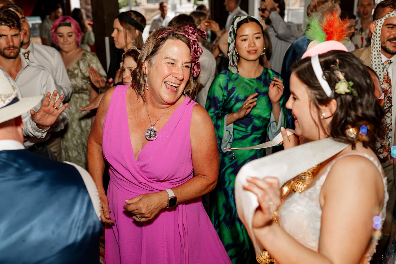 Amidst the vibrant setting of a party, people danced joyfully. In the center, a woman in a pink dress laughed, capturing the evenings joyous energy.