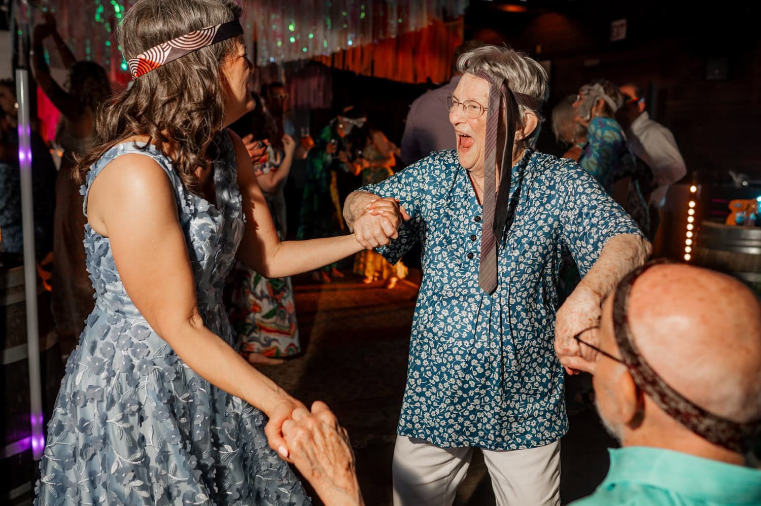 Two women wearing headbands happily dance together at a lively indoor party.