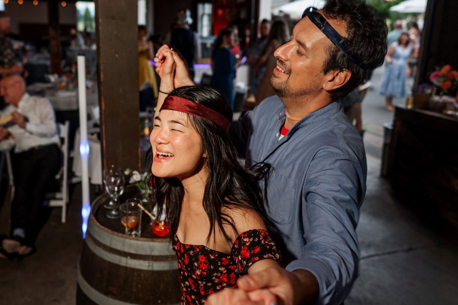 Two people with outstretched arms, wearing headbands, joyfully dancing and smiling in a festive setting at Rossi Farms.