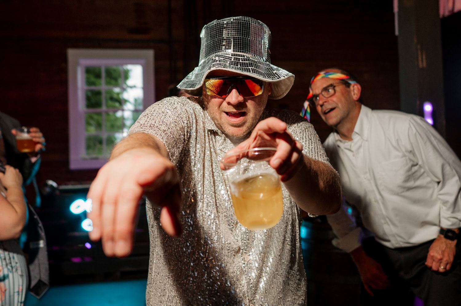 At Rossi Farms, a person in a disco outfit dances with a drink in hand as another person wearing a tie-dye bandana laughs joyfully in the background.