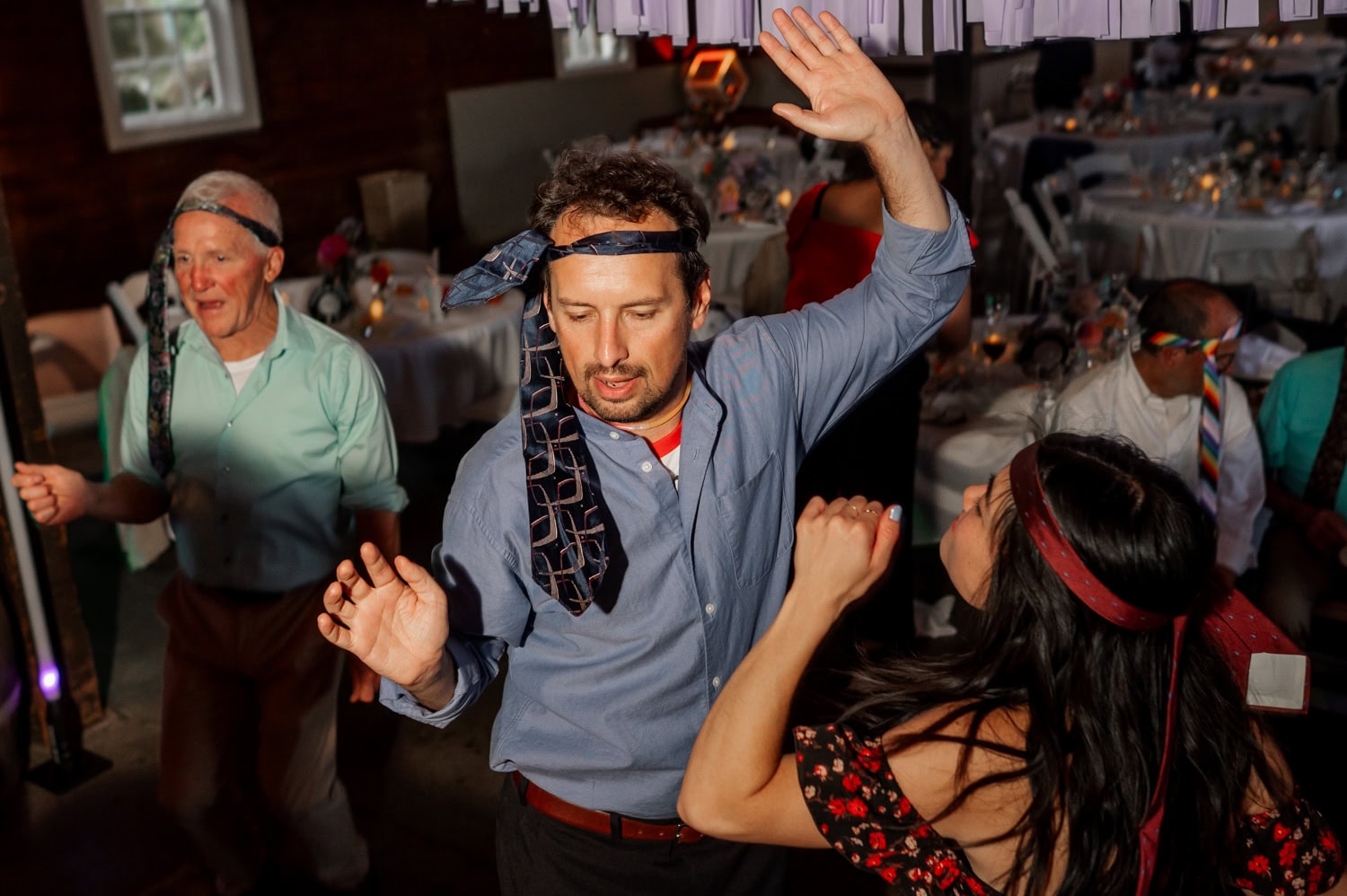 At a lively wedding at Rossi Farms, guests are dancing energetically with ties playfully wrapped around their heads, embodying the celebratory mood.