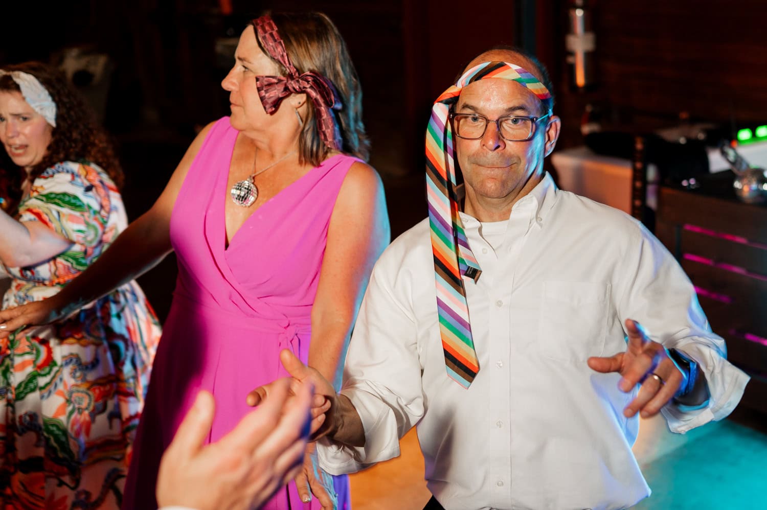 Guests dance joyfully at a lively celebration, colorful ties tied around their heads. Smiles and laughter fill the air, creating a vibrant and energetic atmosphere.