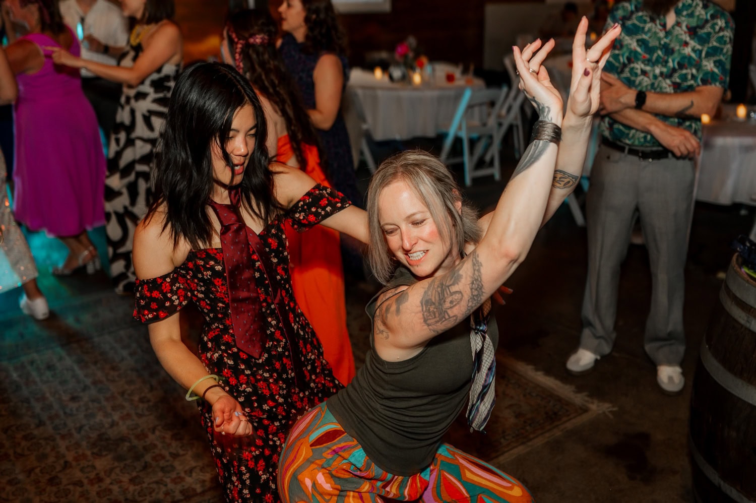Two women dancing energetically at a party, surrounded by other guests and festive lighting, creating a lively scene.