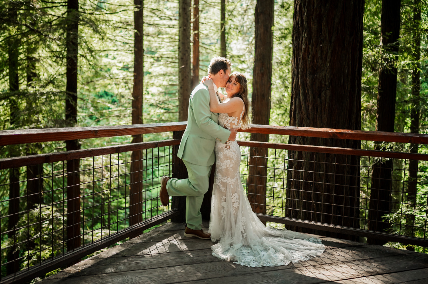 Bride and groom share an intimate kiss on a wooded balcony with tall trees in the background during their Hoyt Arboretum wedding.